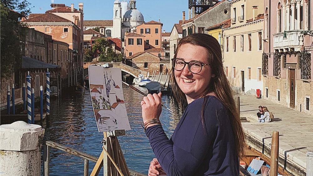 student painting a city scene with river in background